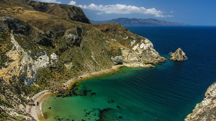 A coved bay with cliffs and turquoise seawater under a blue sky with some clouds