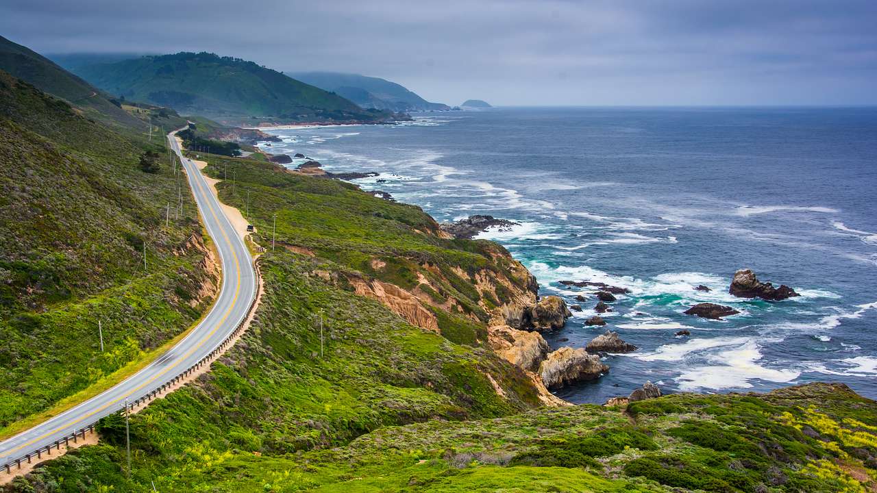 A road winding around a greenery-covered cliff with the ocean to the side