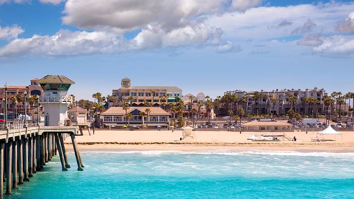 Bright blue ocean with a pier to the side and a sandy shore with buildings on it