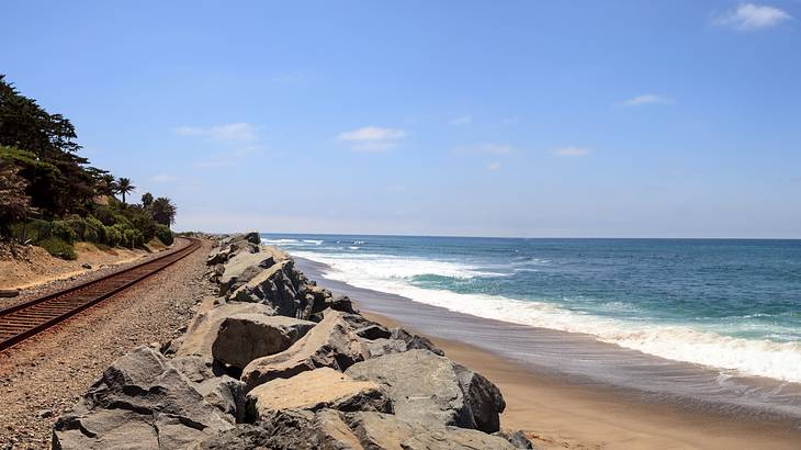 A train track running past a beach under a blue sky