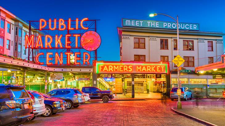 A market at night with cars in front and red neon signs on the buildings