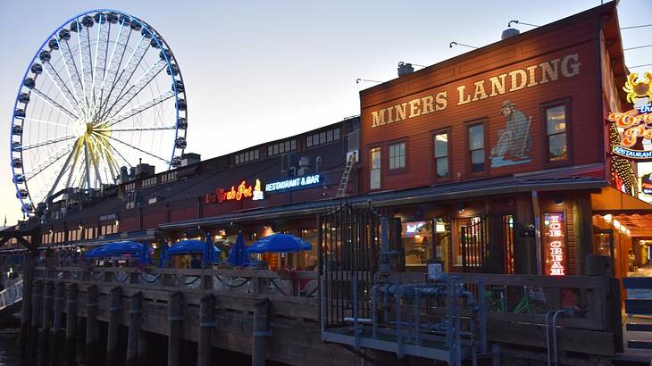 A pier with a Ferris Wheel and a building that says "Miners Landing" at night