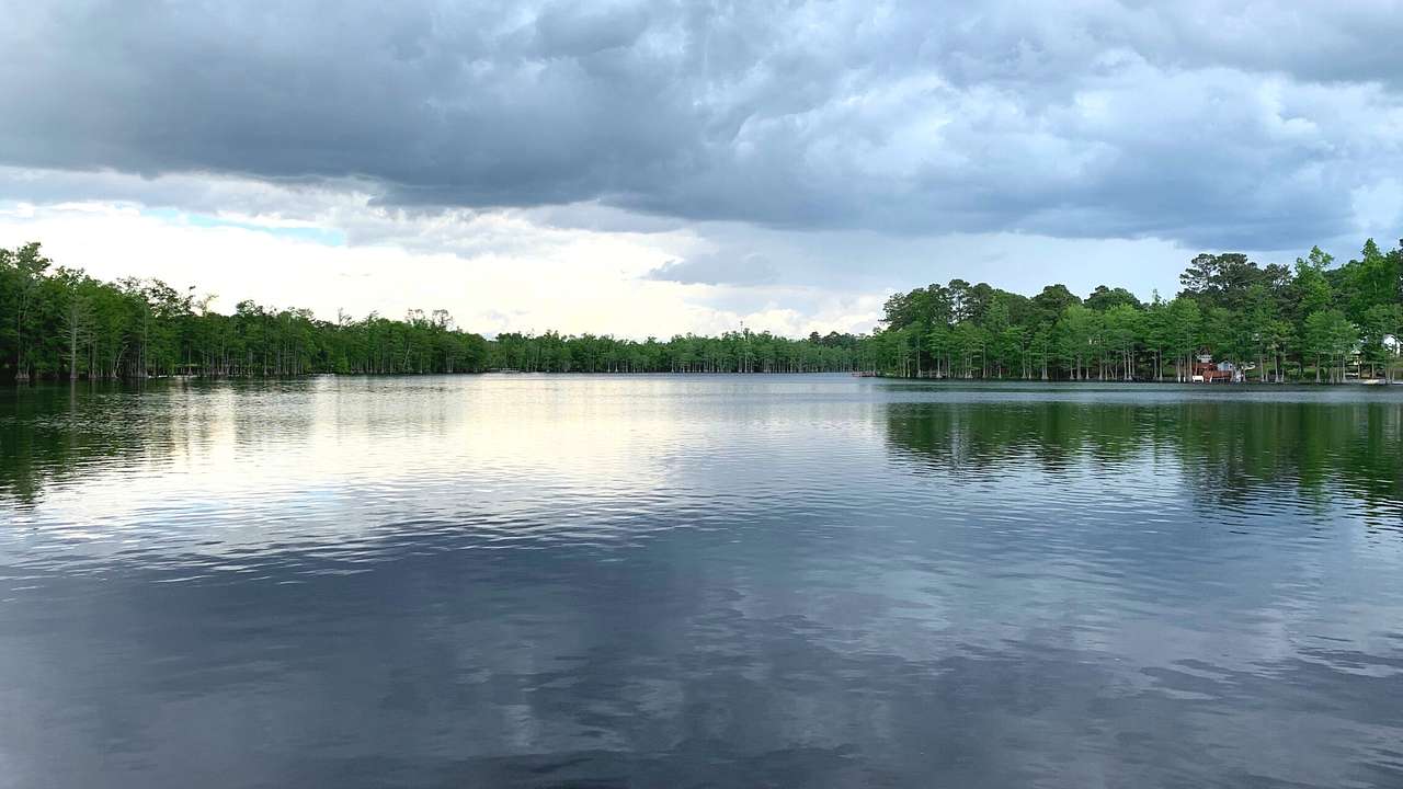 A lake with trees on the shore under a cloudy sky