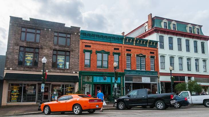 Small buildings on a street with cars parked in front of them under a cloudy sky