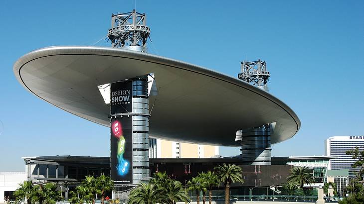 A shopping mall with an oval roof and palm trees in front under a blue sky