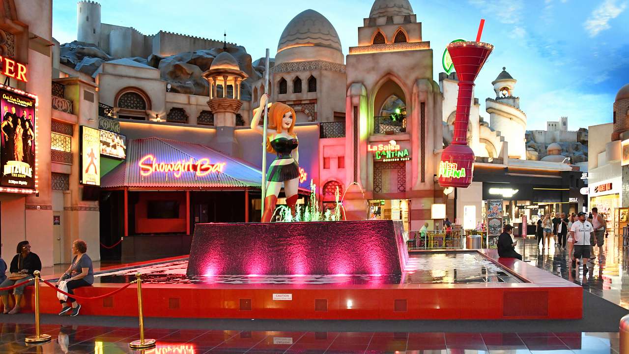 An indoor mall with a fountain, red lights, and tall cartoon statues