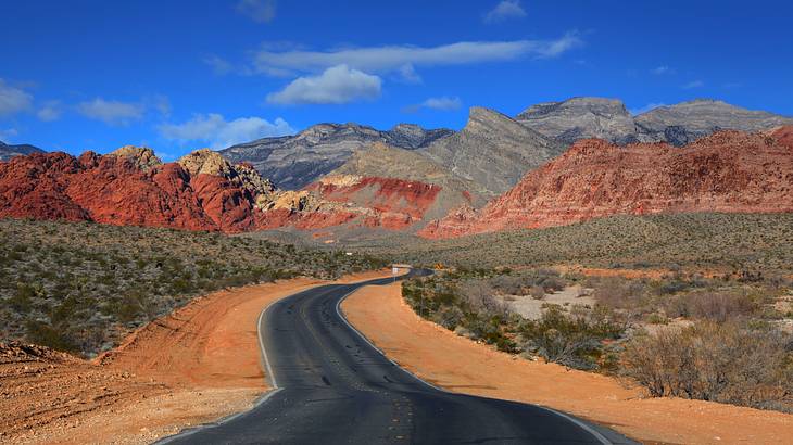 A winding road going through a desert to a red rock mountain range