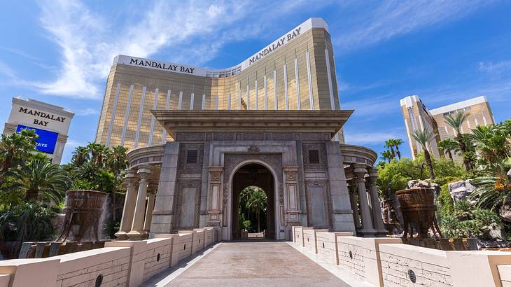 A stone walkway leading to an arch with a gold mirrored hotel building behind