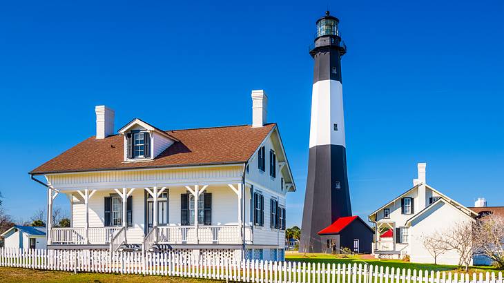 A small white house with a black and white lighthouse and other buildings next to it.