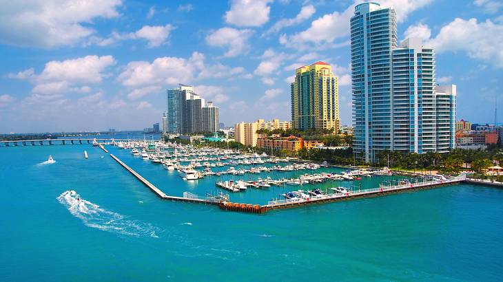 A marina and skyscrapers surrounded by blue ocean under blue sky with clouds