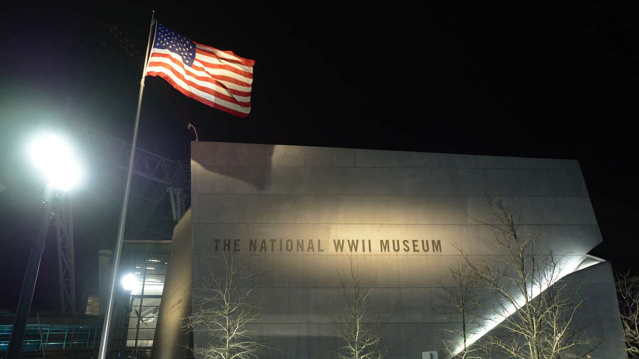 Grey building with words "The National WWII Museum" with a US flag - nighttime