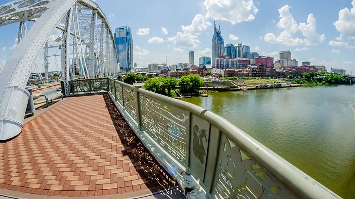 Walkway on a bridge along a body of water, buildings and skyscrapers in the distance