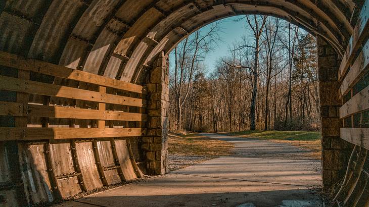 Covered wooden bridge and stone walkway leading to a trail with grass and trees