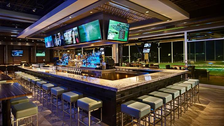 A bar with tv screens above it and an indoor golf course to the side