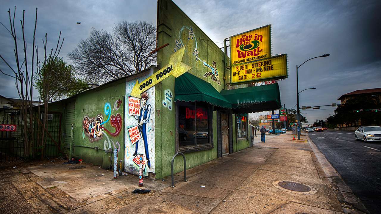 The exterior of a bar that's painted green and has yellow signs and graffiti on it