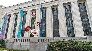 A stone museum building with colorful banners and rose sculptures in front of it