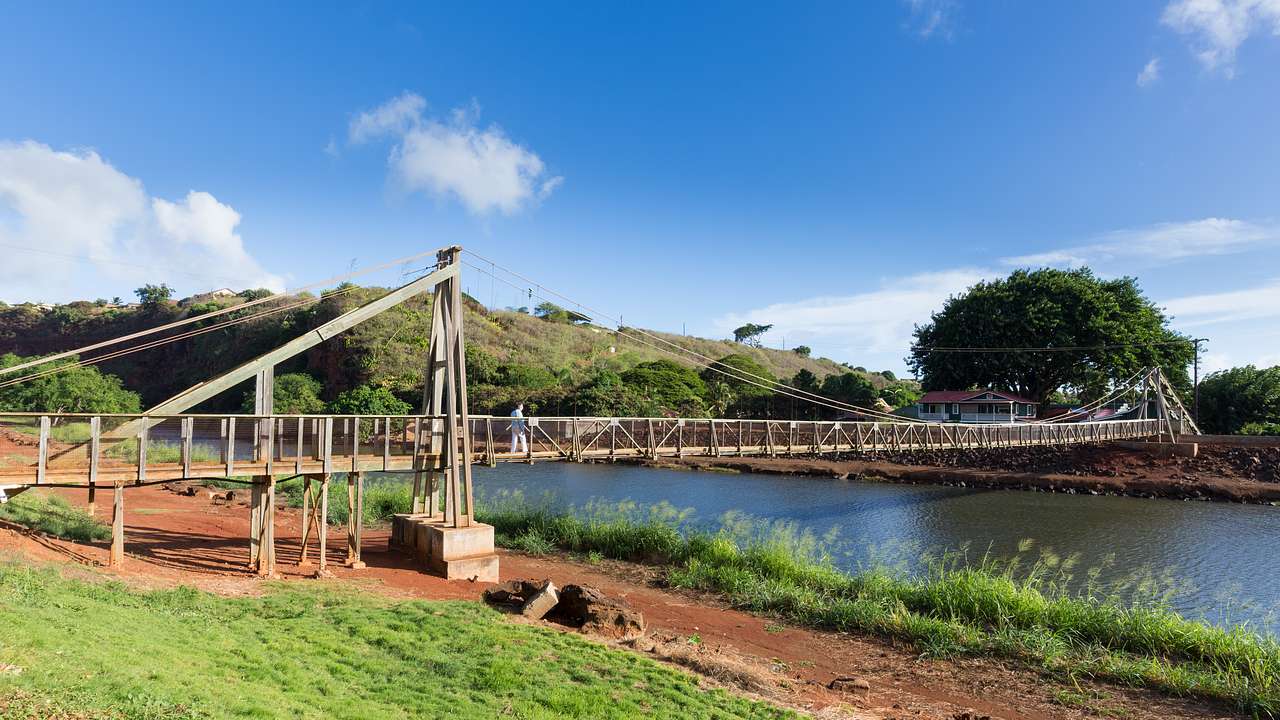 A wooden suspension bridge over a river with grass and mud on the banks