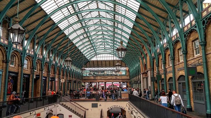 Inside a market with a green arched open roof and many visitors