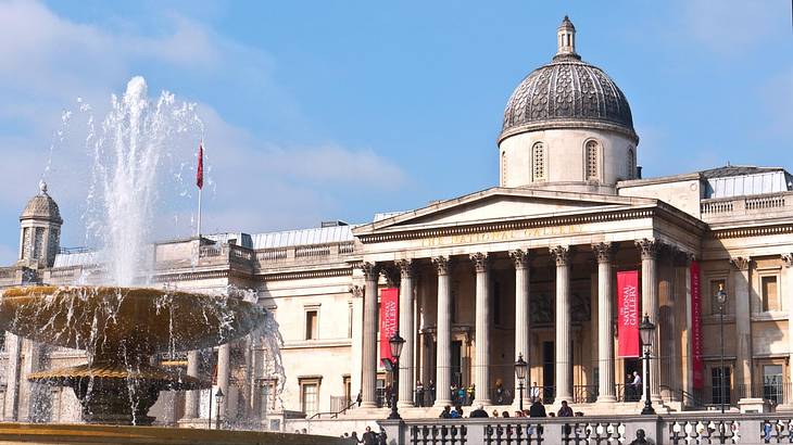 A fountain with water shooting upwards against a neoclassical building with a dome