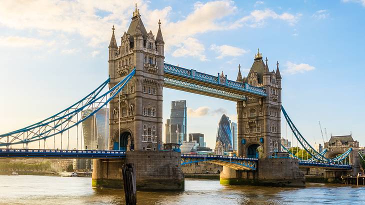 A bridge with gothic towers over a river and against skyscrapers and blue sky