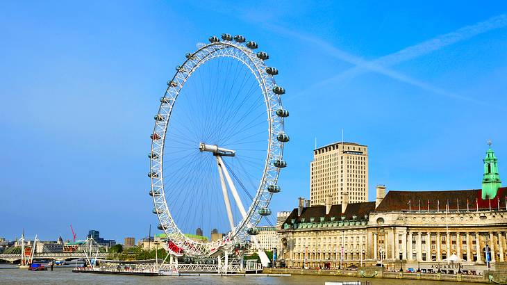 Looking up at a white Ferris Wheel beside an old building, under a clear blue sky