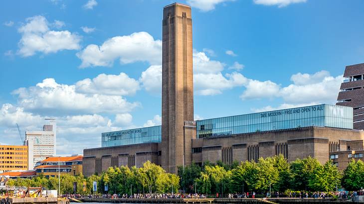 A modern brown building with a tall tower in the middle, against a partly cloudy sky