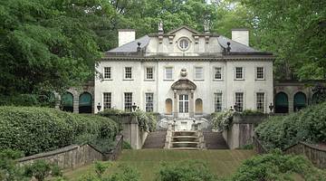 A white manor house with steps in front of it and greenery surrounding it