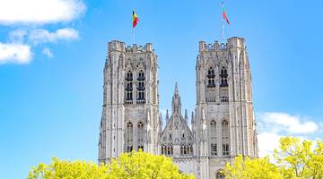 Two tall towers of a cathedral with flags on top against a blue sky