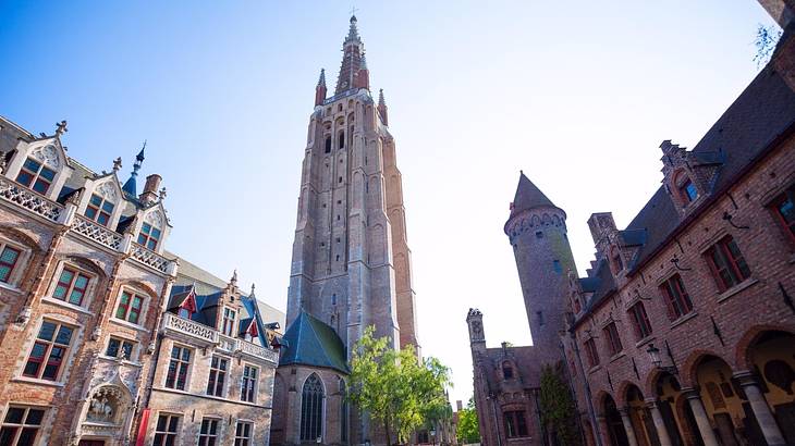 A tall church tower with greenery at its foot in between two buildings on a clear day