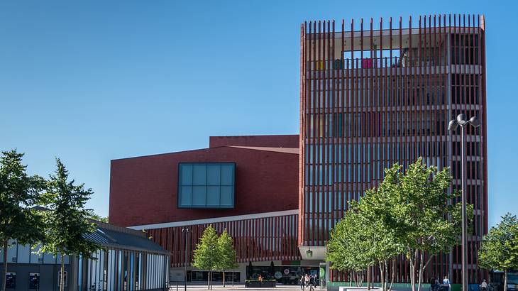 The exterior of a modern red building complex surrounded by trees and a few people