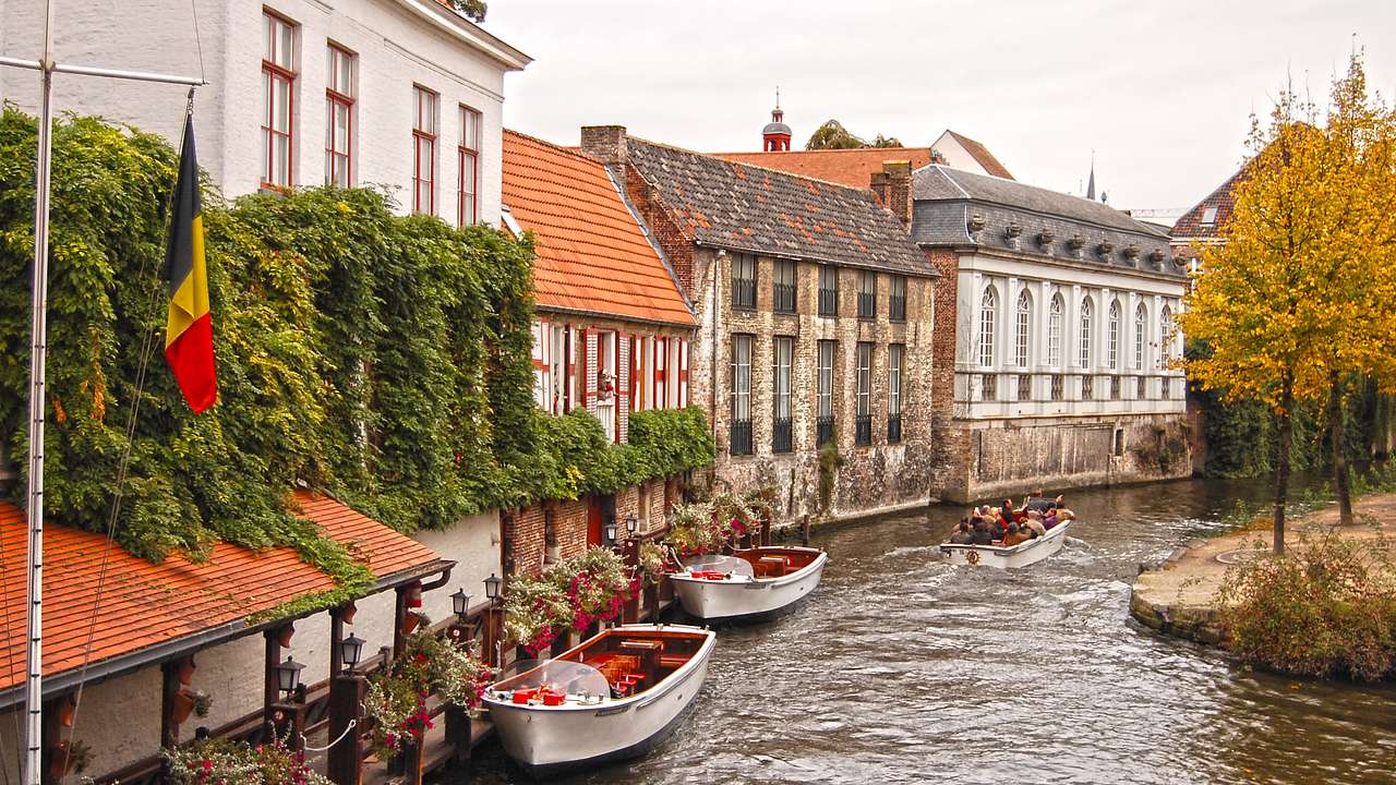 People in a boat on a canal with old buildings and a Belgian flag on the left