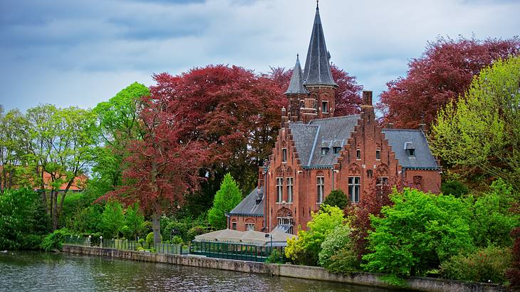 Gothic style, grey roofed castle surrounded by greenery, overlooking a lake