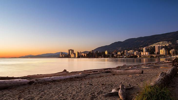 View of a beach, city and mountain in background at sunset, BC, Canada