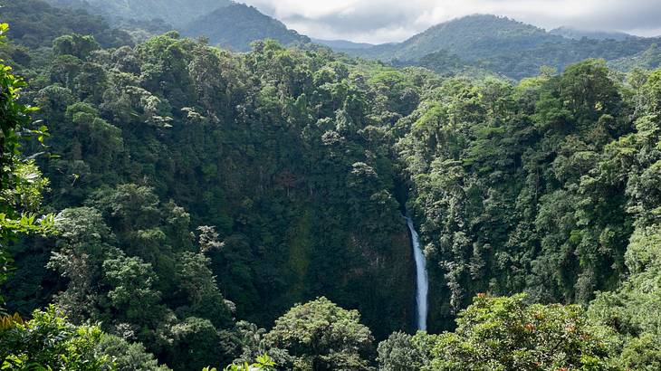 A waterfall in the jungle with mountains and clouds in the background