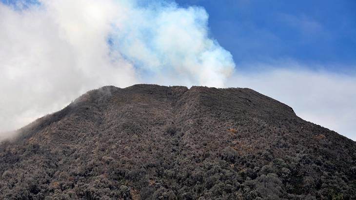 View of a volcano crater erupting white fumes into the blue sky