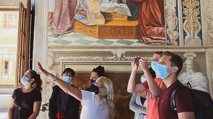 Individuals on a tour wearing masks, looking at famous paintings on a room's walls
