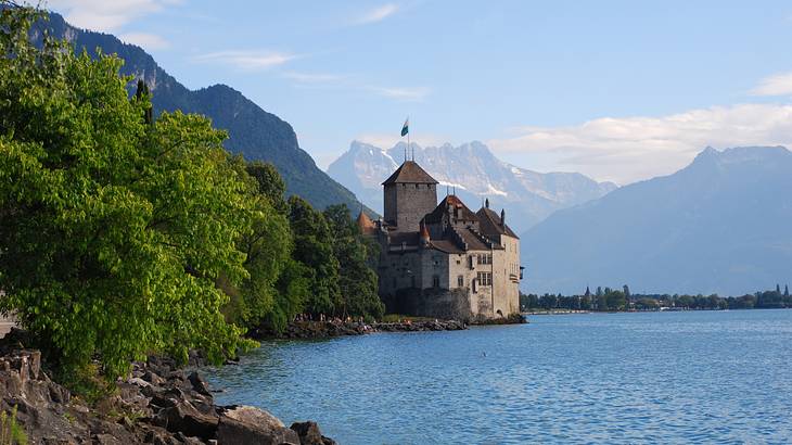 A chateau on a lake surrounded by green trees and mountains, Switzerland