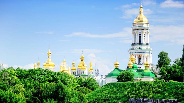 The gold pointy rooftops of a monastery from behind green trees
