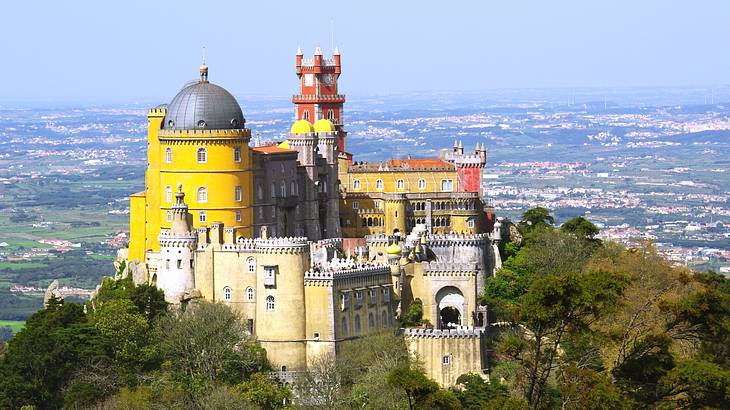 A colourful castle on a tree-filled hill overlooking a city from above