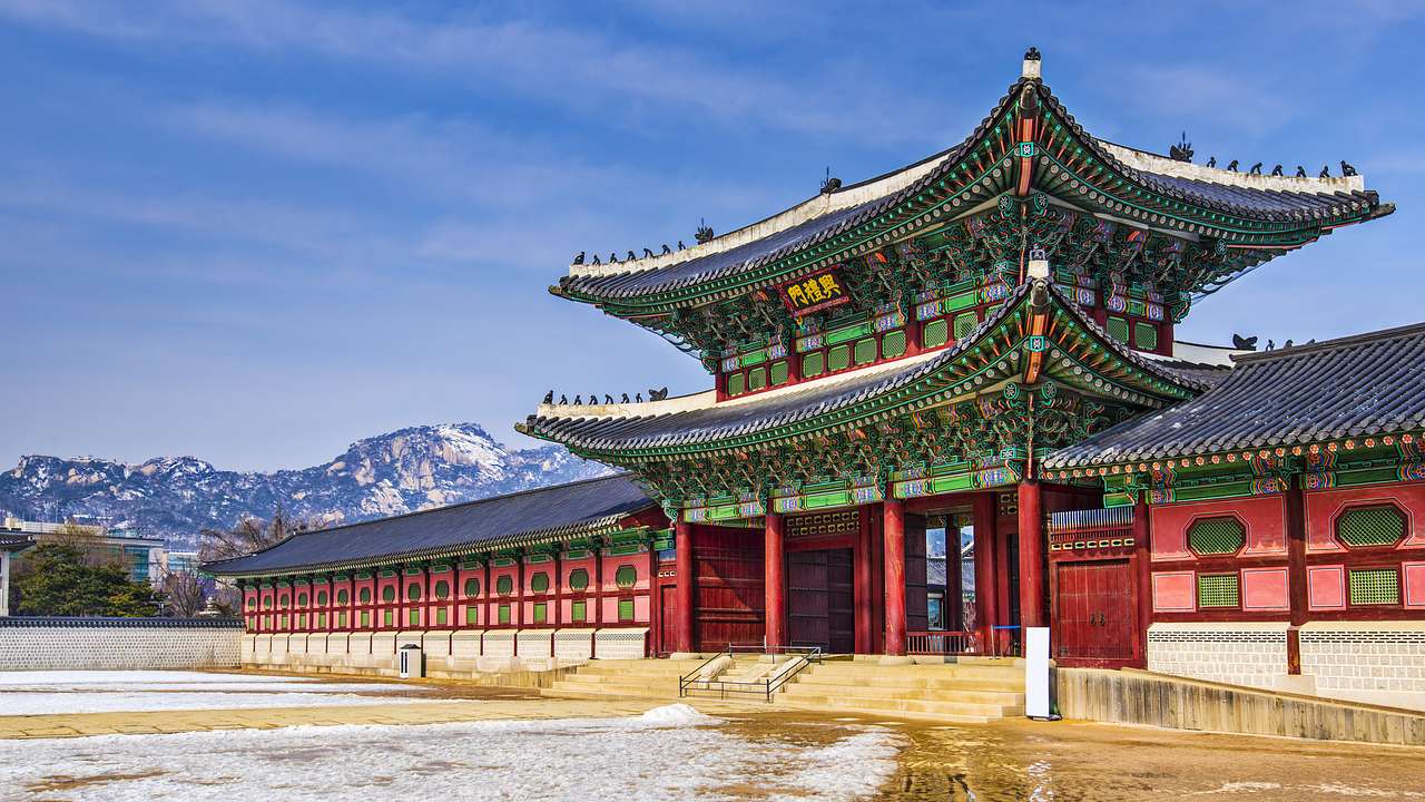 An Asian-style temple building with red and green details and a mountain at the back