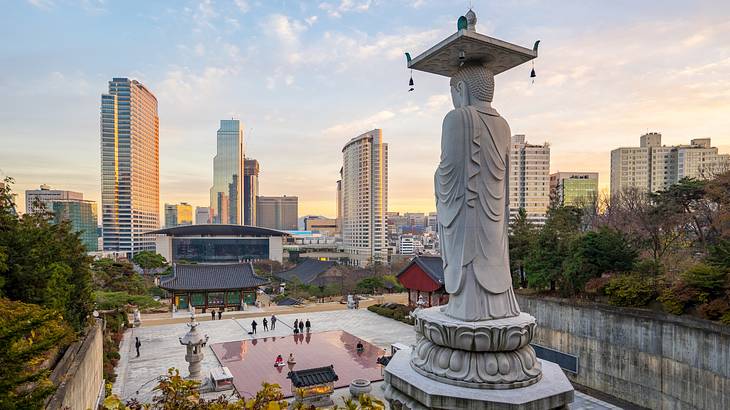 A stone statue overlooking a square and skyscrapers at sunset