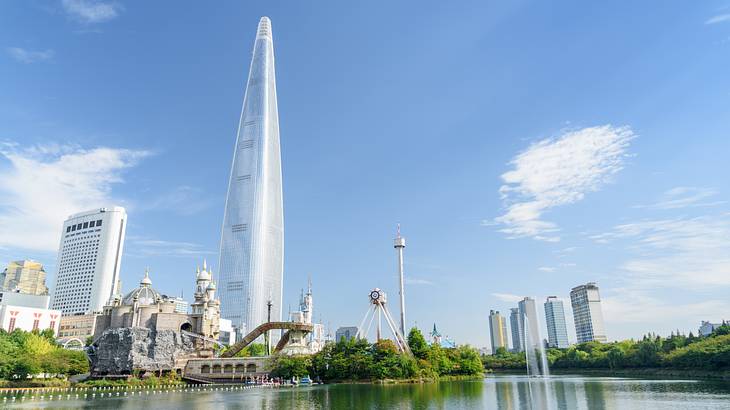 A tall mirrored tower next to other buildings, green trees and a body of water