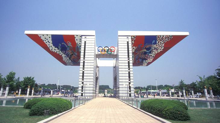 An arch-type winged structure with a path running through it, with greenery around