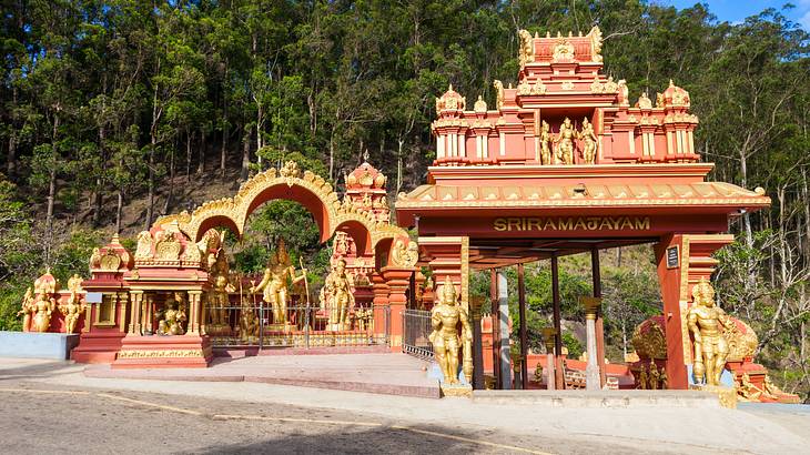 A brightly coloured peach temple with many statues and trees at the back