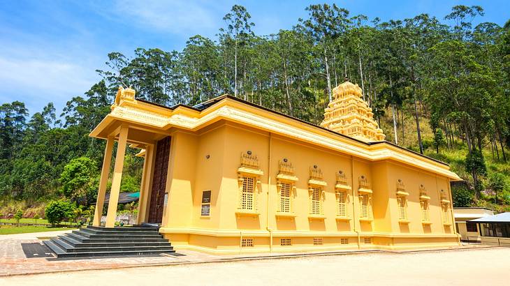 A long yellow temple from the side with a staircase and trees behind