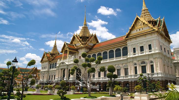 A temple with pointed gold roofs next to greenery on a partly cloudy day