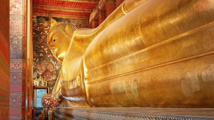 A giant gold reclining Buddha statue in a temple with red walls