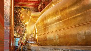 A giant gold reclining Buddha statue in a temple with red walls