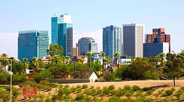 A city skyline with trees in front of it under a blue sky