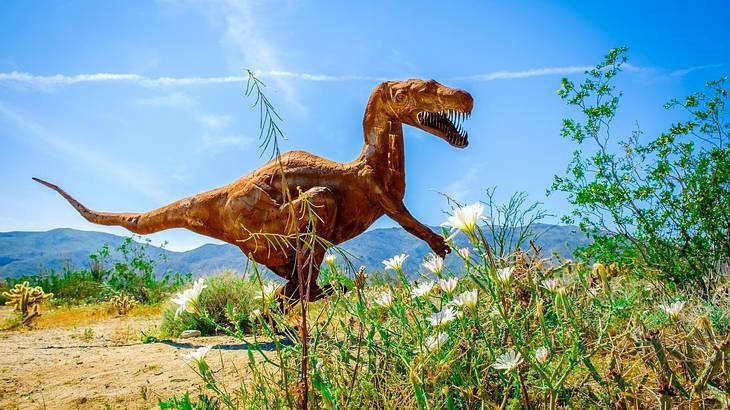 A T-rex sculpture in a desert with some greenery in the foreground